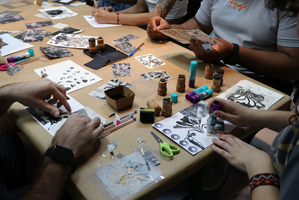 Imagem de várias pessoas desenhando em cima de uma mesa. O plano é detalhe e está focado nas mãos.